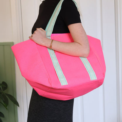 Person holding a pink tote bag with green straps against a white wall.