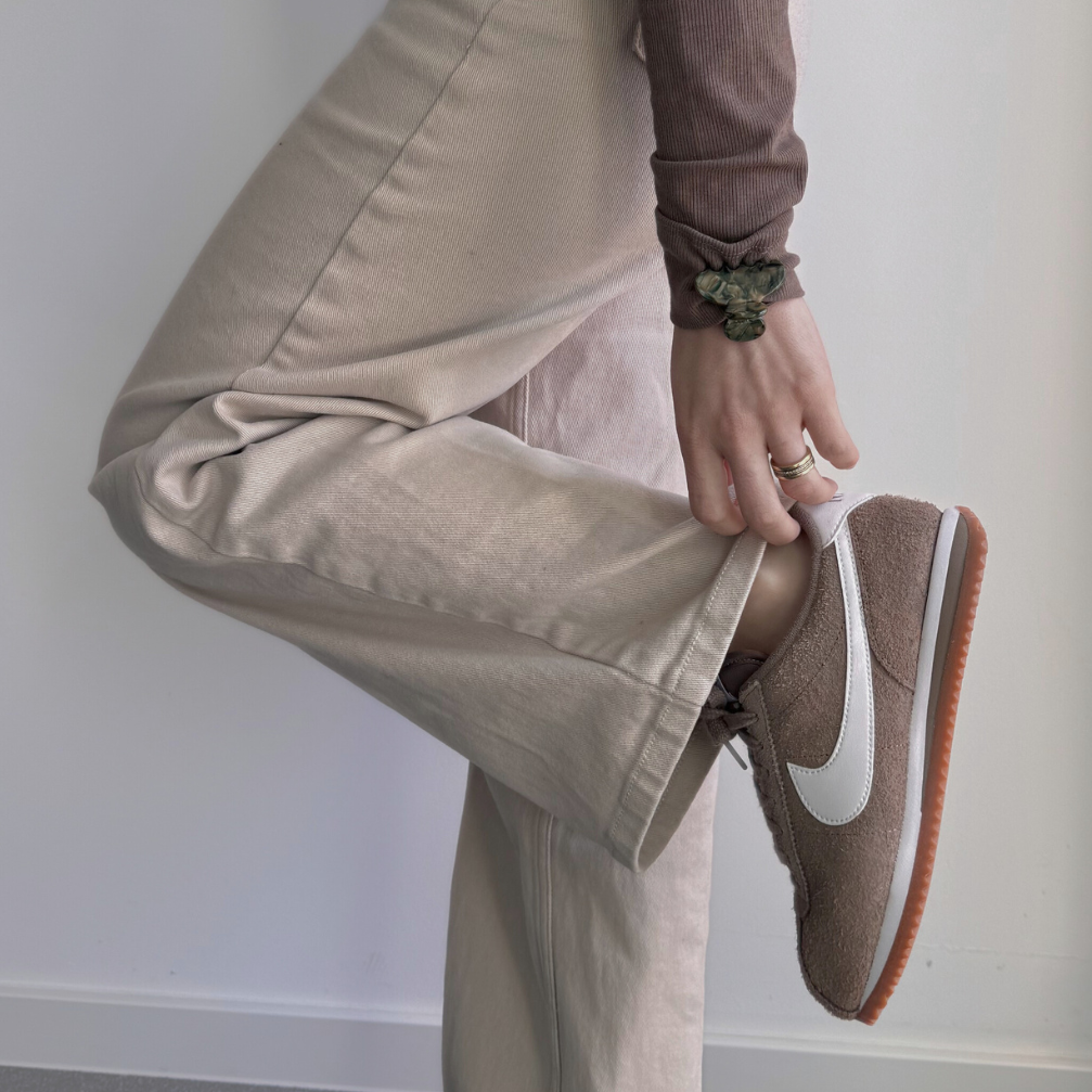 Person wearing beige pants and brown sneakers with a white logo, and a hair clip on wrist.