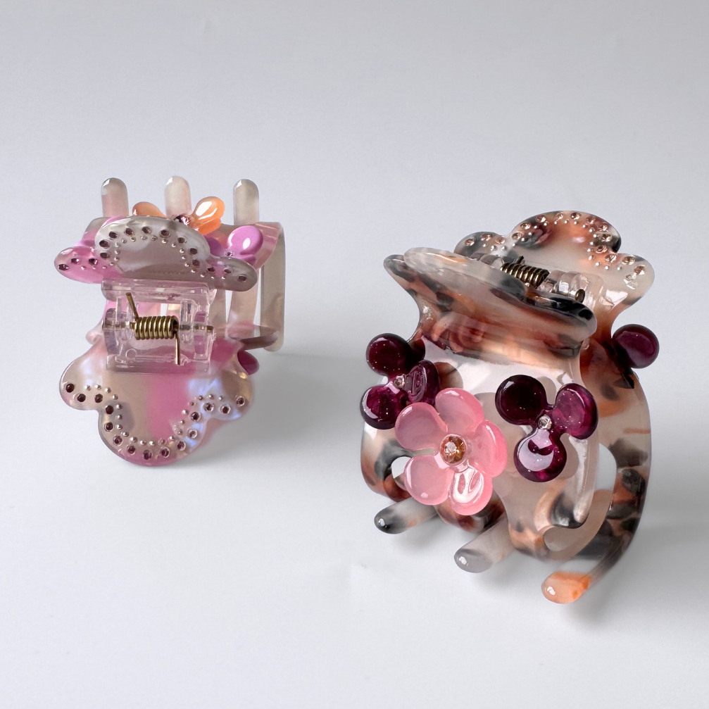 Pair of decorative hair clips with floral designs on a light gray background