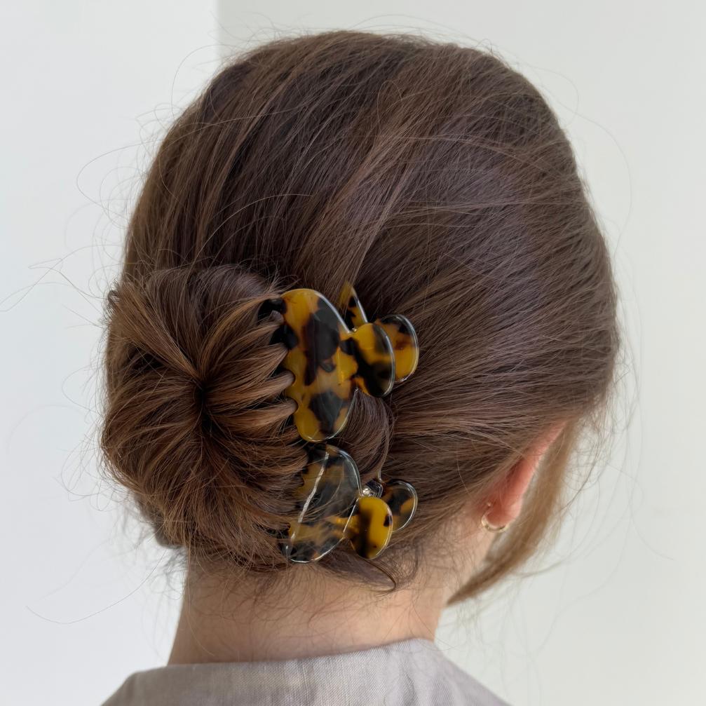 Person with a bun holding yellow hair clips against a white background