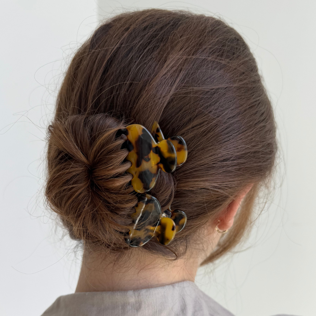 Person with a bun holding yellow hair clips against a white background
