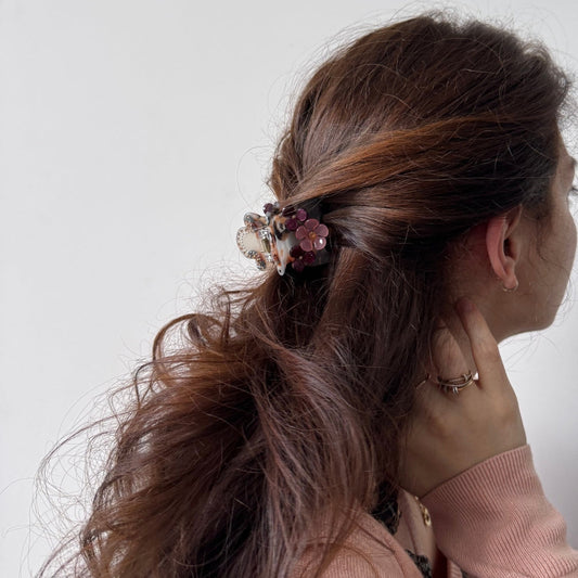 Woman with a ponytail wearing a pink sweater and floral hairclip against a white background
