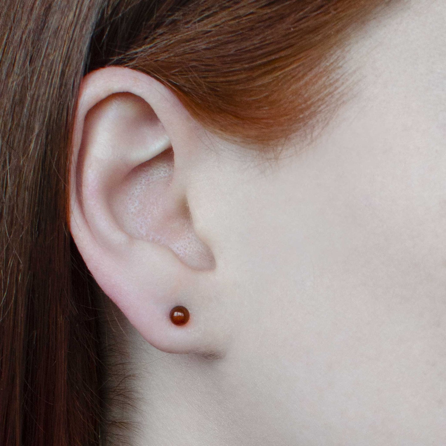 Woman wearing tiny Carnelian gemstone ball stud earring in earlobe