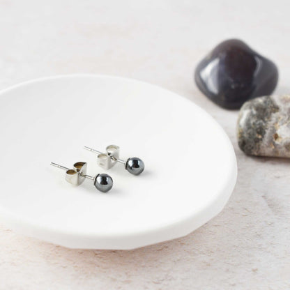 Tiny dark grey Hematite gemstone stud earrings laying in white trinket dish.