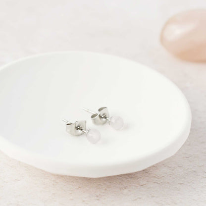 Tiny pale pink Rose Quartz stud earrings laying in white trinket dish.