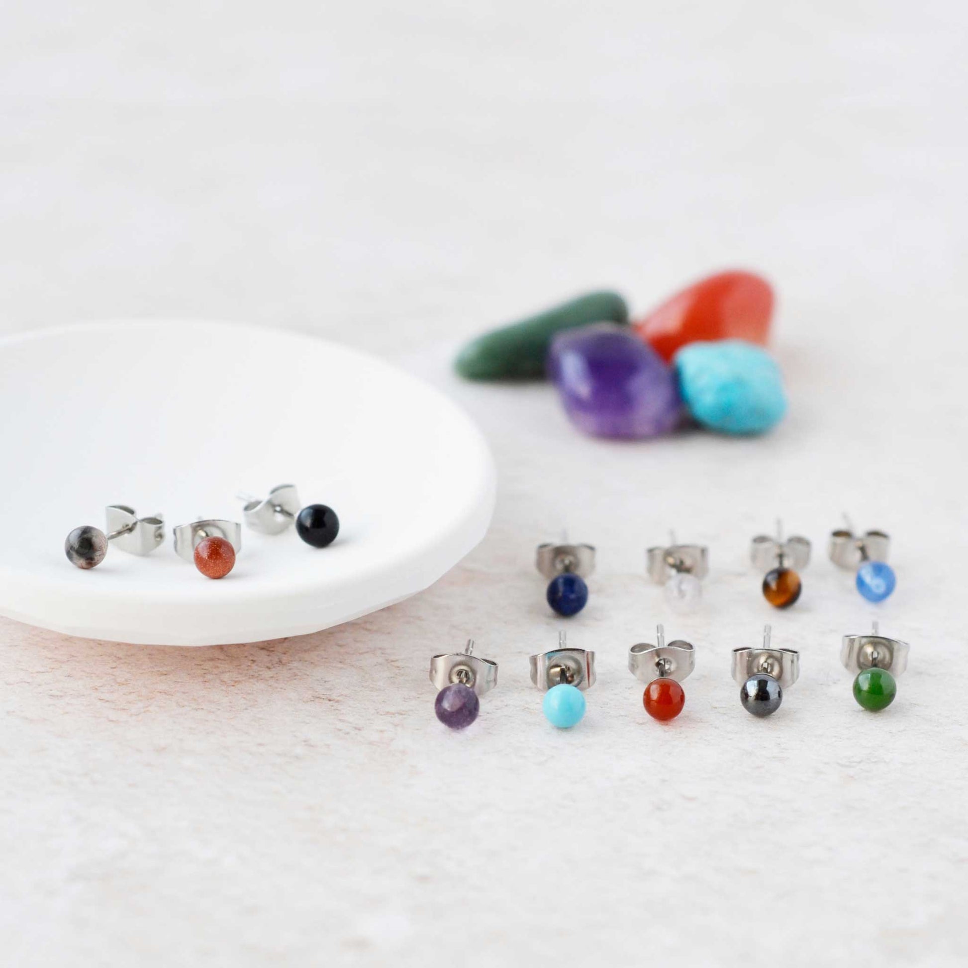 Tiny coloured gemstone stud earrings displayed next to trinket dish.