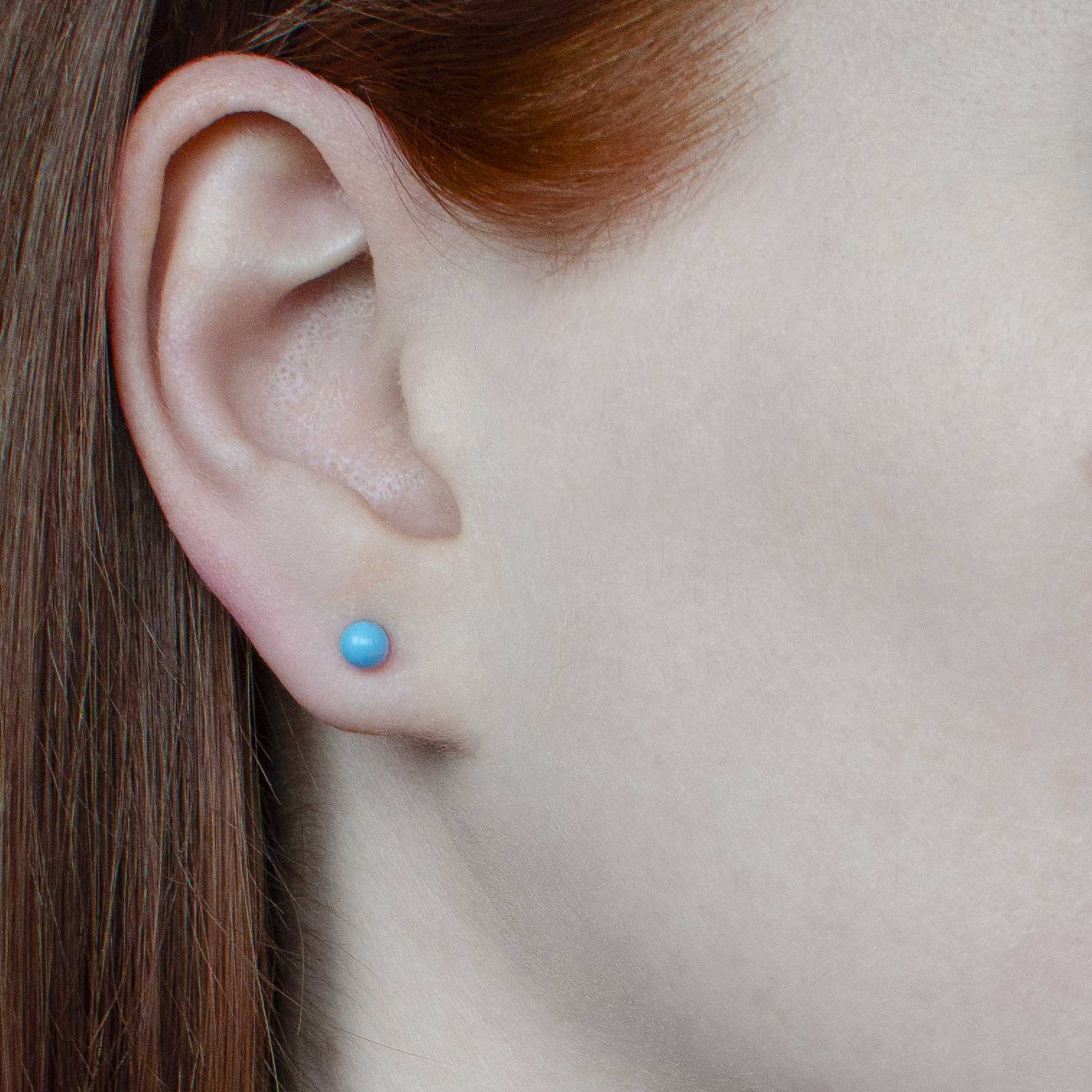 Woman wearing tiny Turquoise gemstone stud earring in earlobe