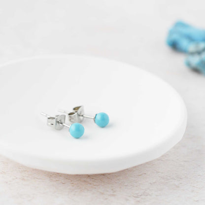 Tiny Turquoise ball stud earrings laying in white trinket dish.