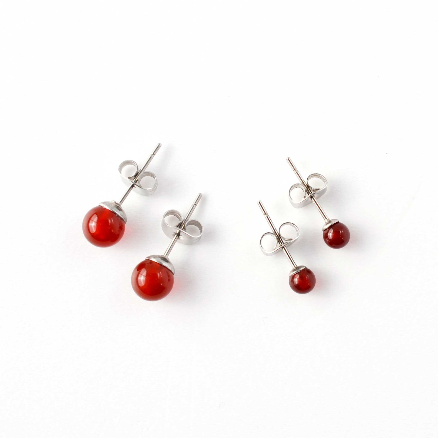 Small and large Carnelian stud earrings laying on white background.