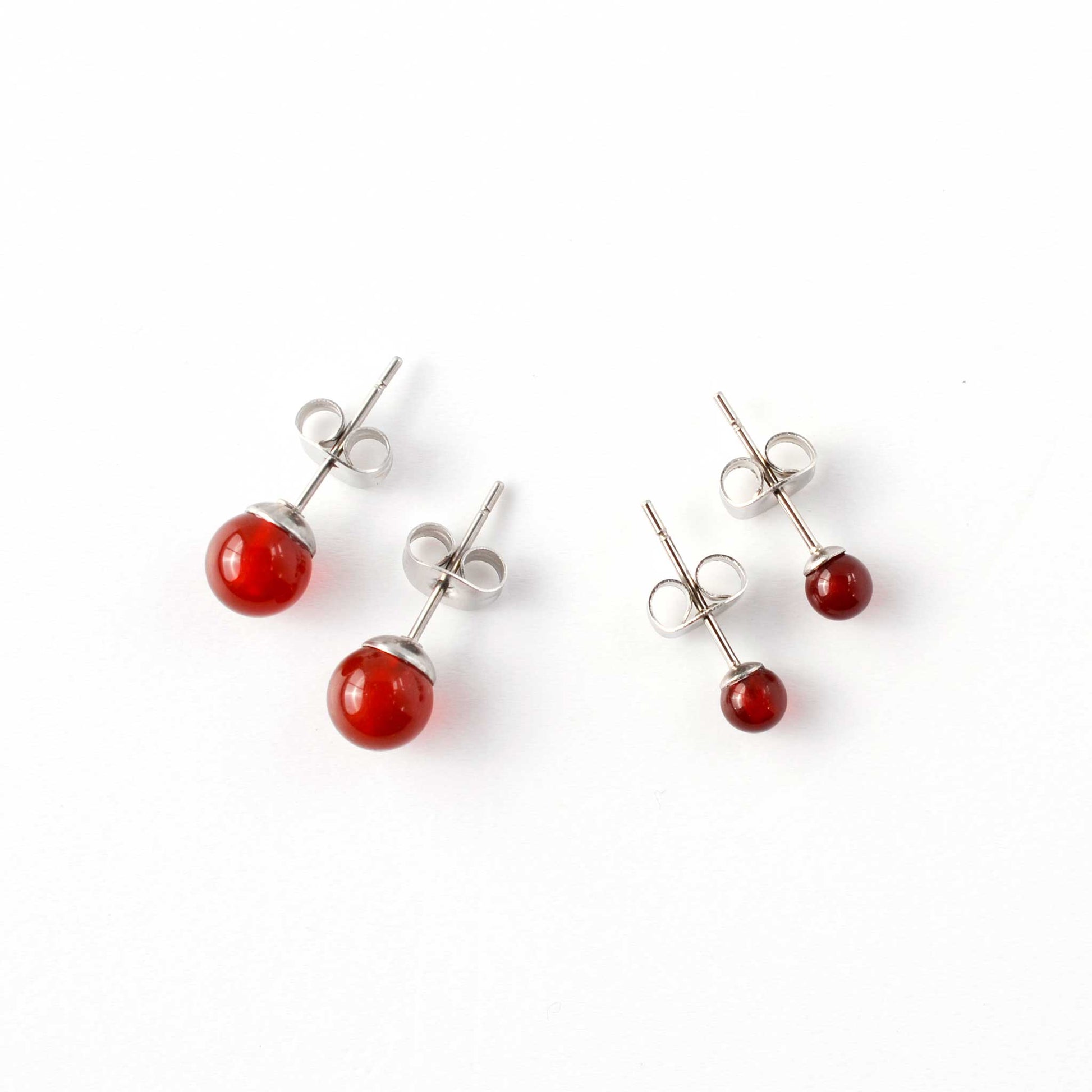 Small and large Carnelian stud earrings laying on white background.