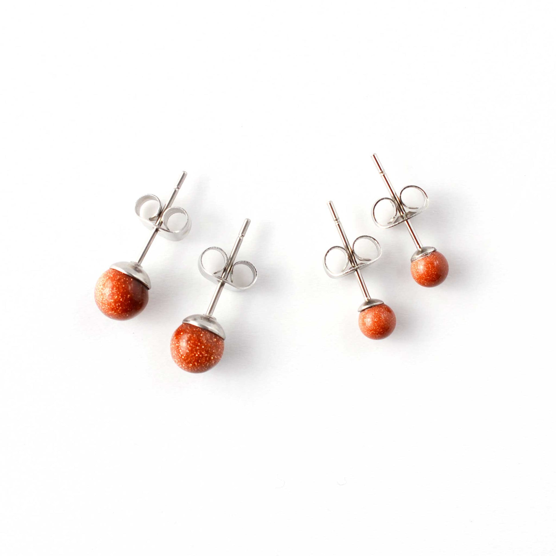 Small and large Goldstone gemstone stud earrings laying on w hite background.
