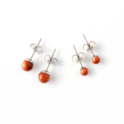 Small and large Goldstone gemstone stud earrings laying on w hite background.