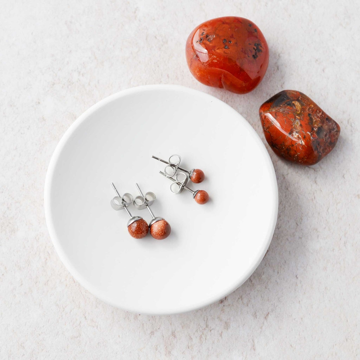 Two pairs of Goldstone gemstone studs laying in a white trinket dish.