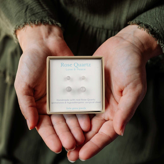Hands holding a box of Rose Quartz earrings with a blurred background