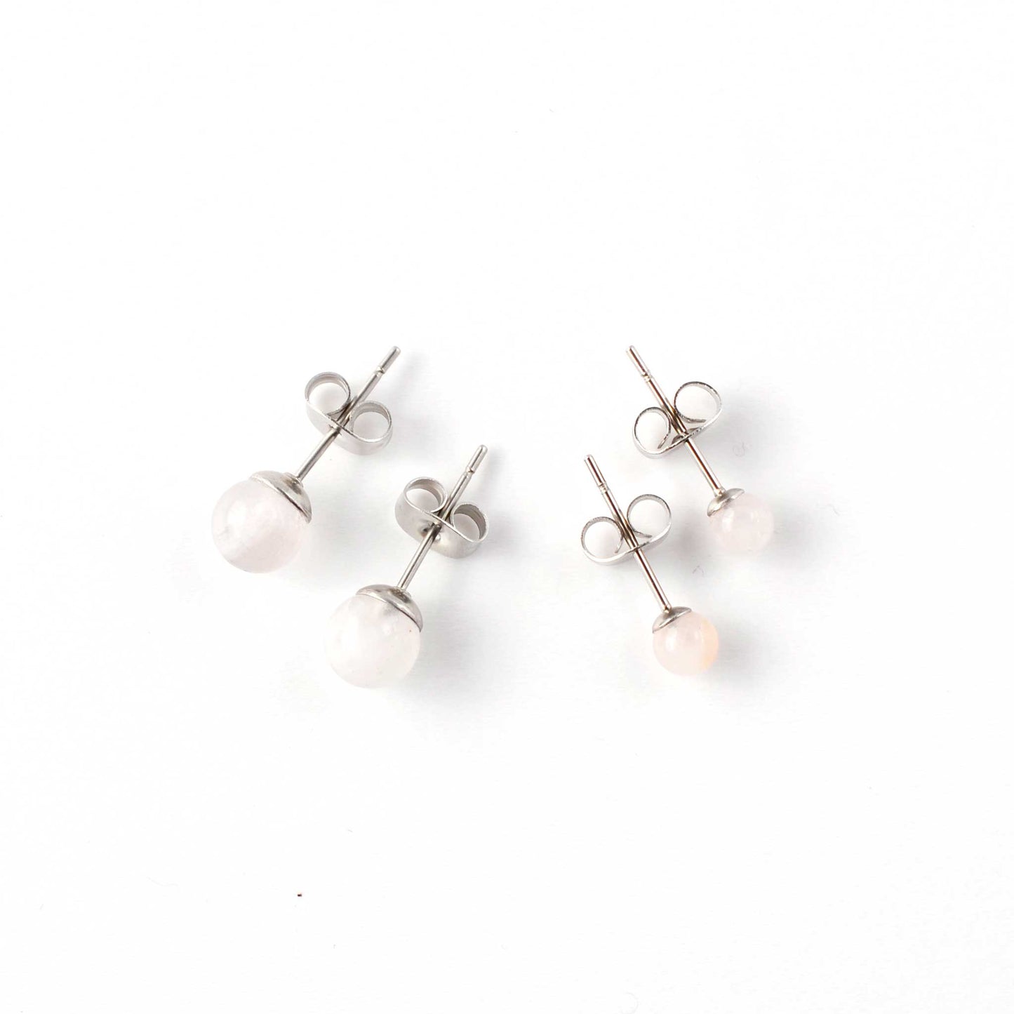 Small and large Rose Quartz stud earrings laying on white background.