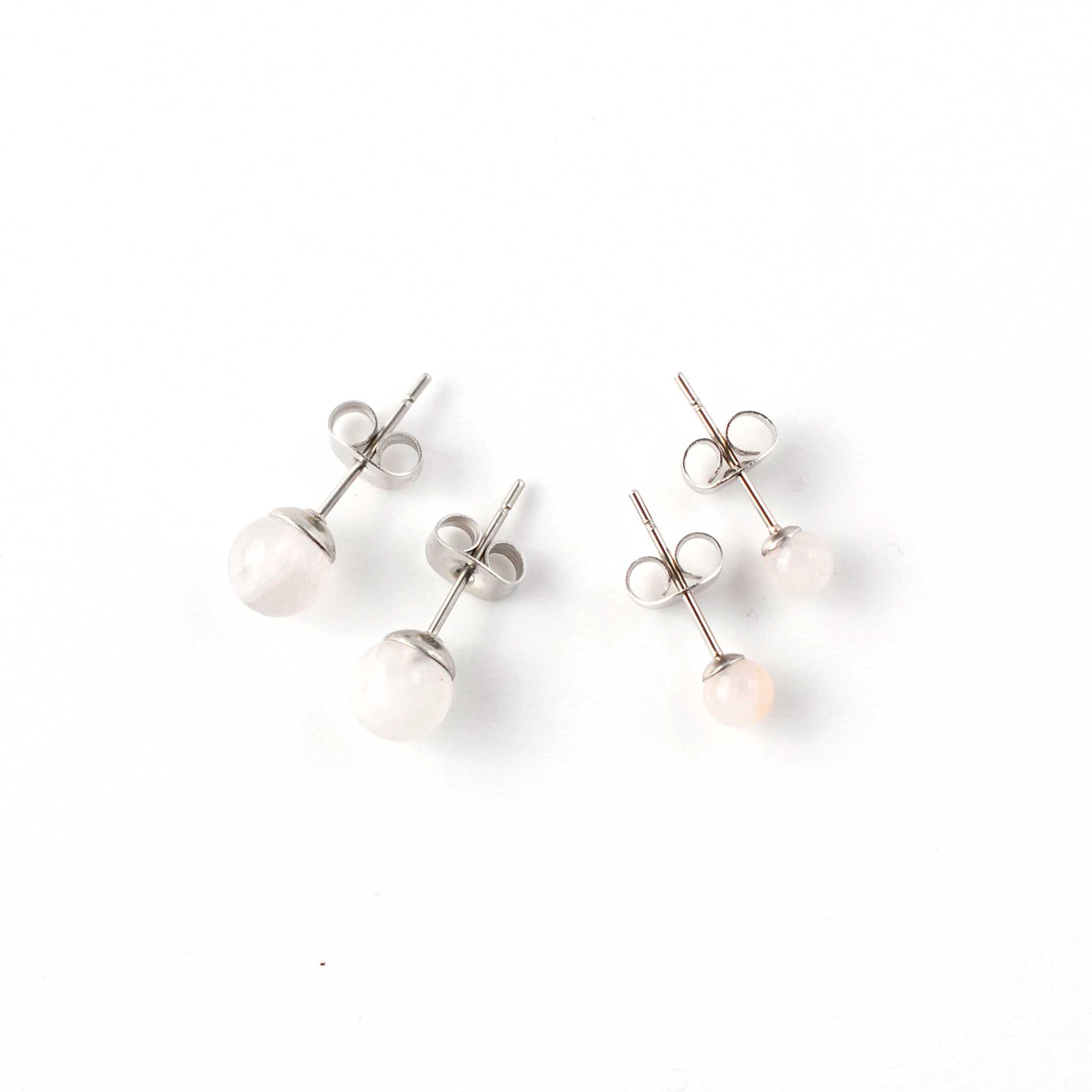 Small and large Rose Quartz stud earrings laying on white background.