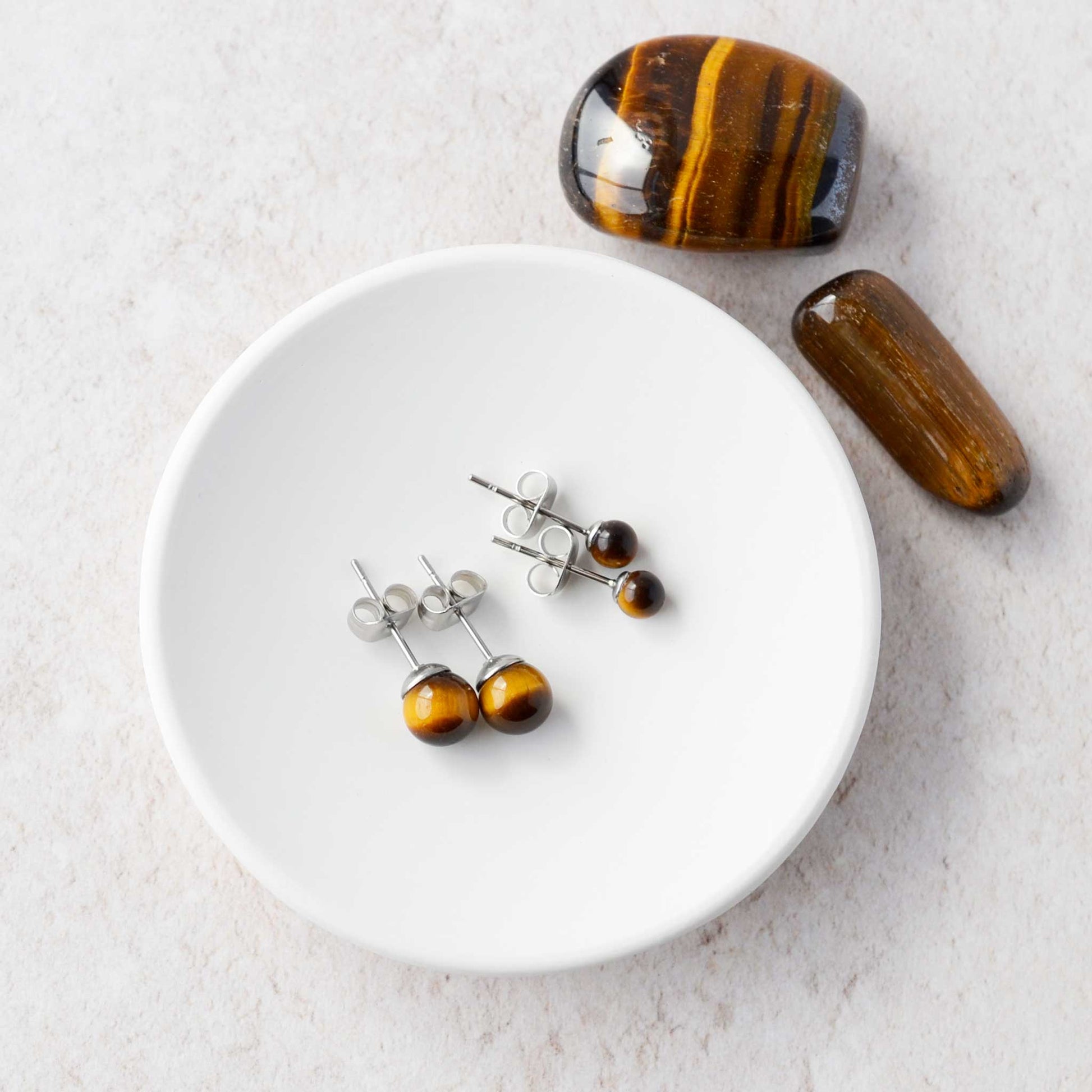 Two pairs of Tiger's Eye stud earrings laying in a white trinket dish.