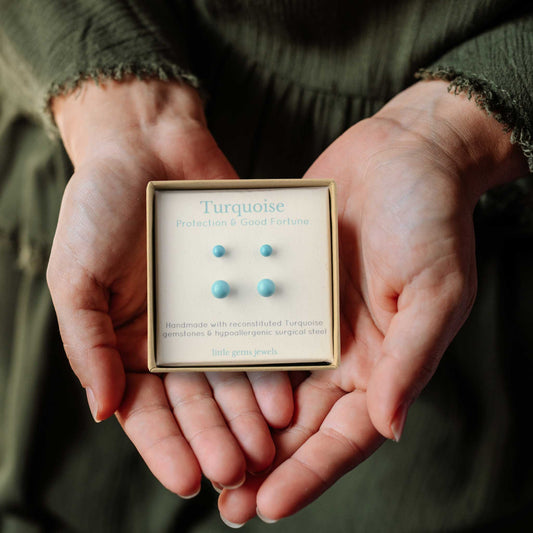 Hands holding a box of turquoise stud earrings with a blurred background