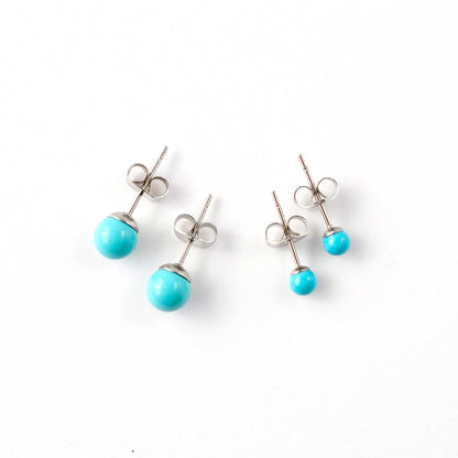 Small and large Turquoise stud earrings laying on white background.