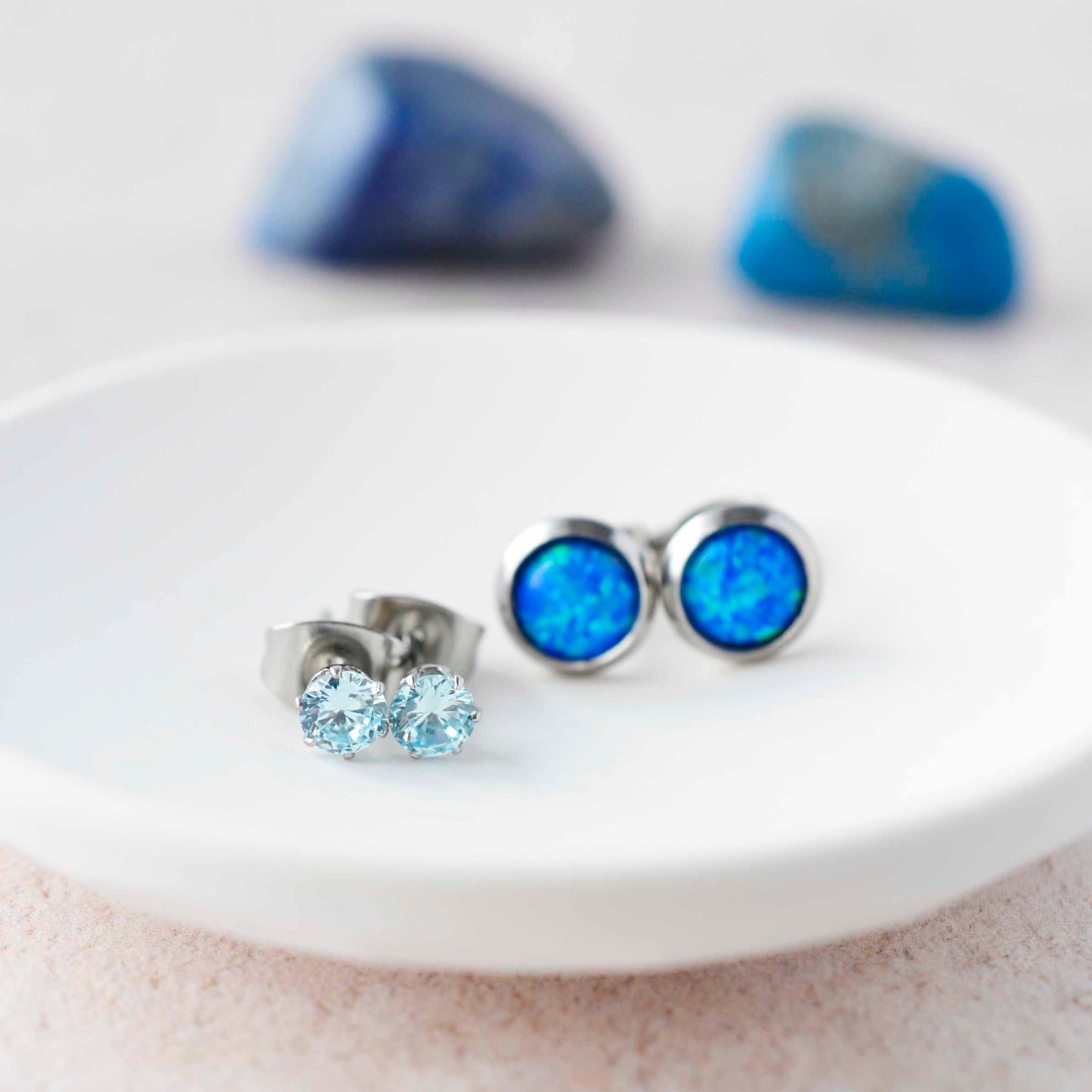 Aqua CZ studs and blue lab opal stud earrings sitting in small white trinket dish.