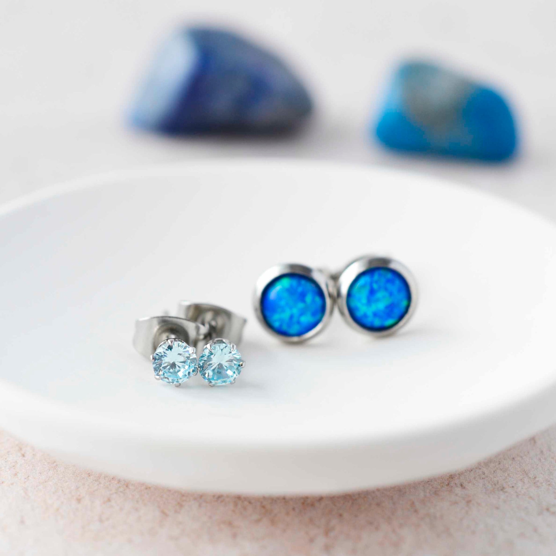 Aqua CZ studs and blue lab opal stud earrings sitting in small white trinket dish.