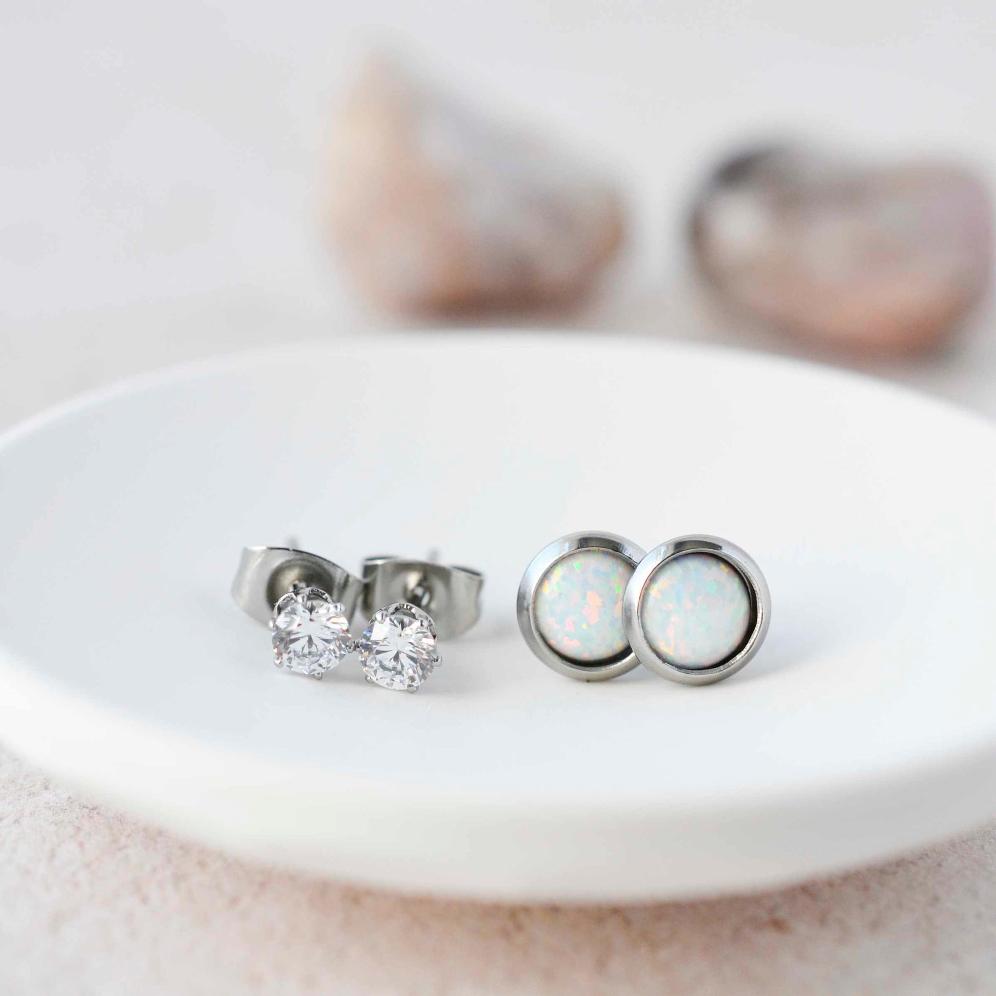 Clear CZ studs and white lab opal stud earrings sitting in small white trinket dish.