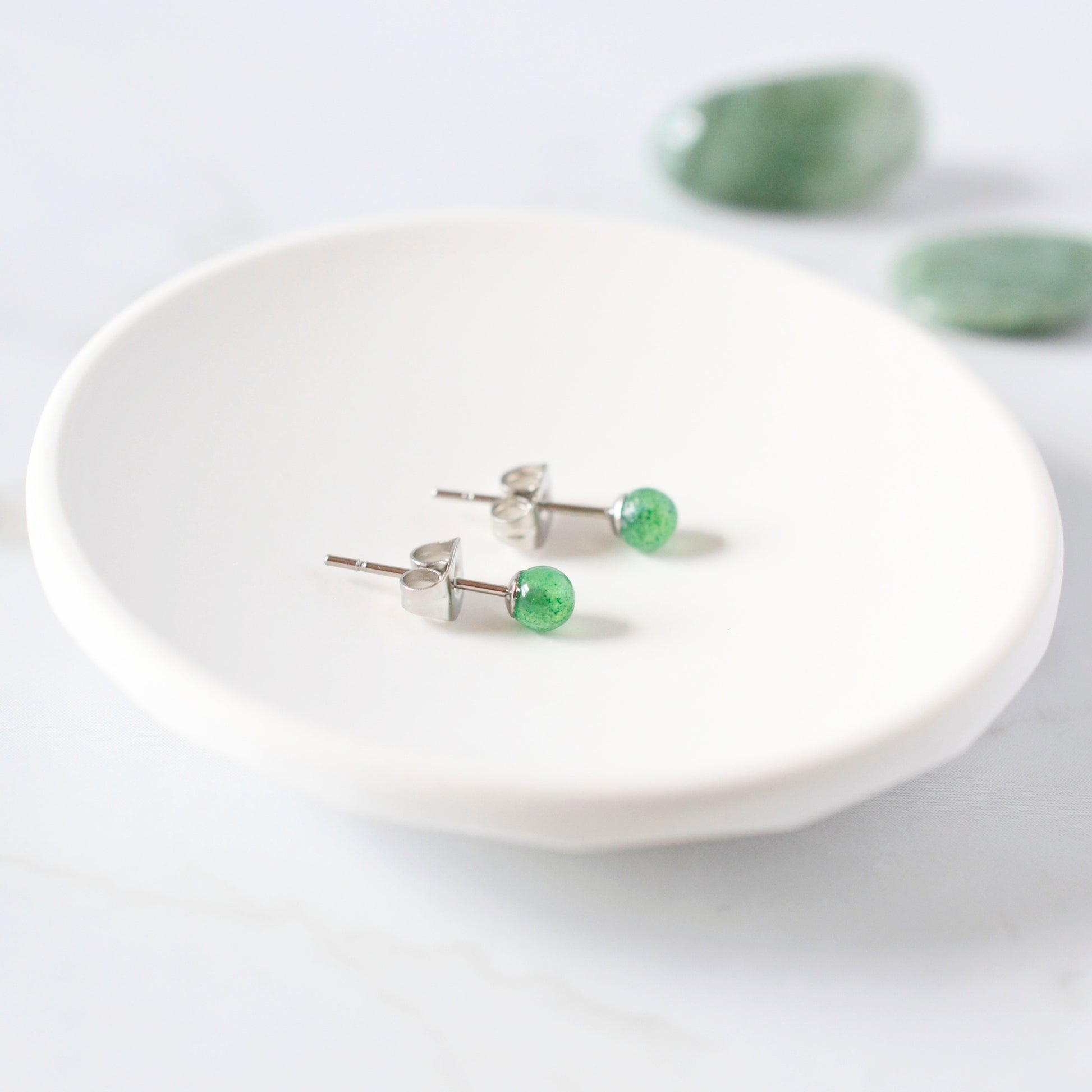 Green stone earrings on a white trinket dish with a light background