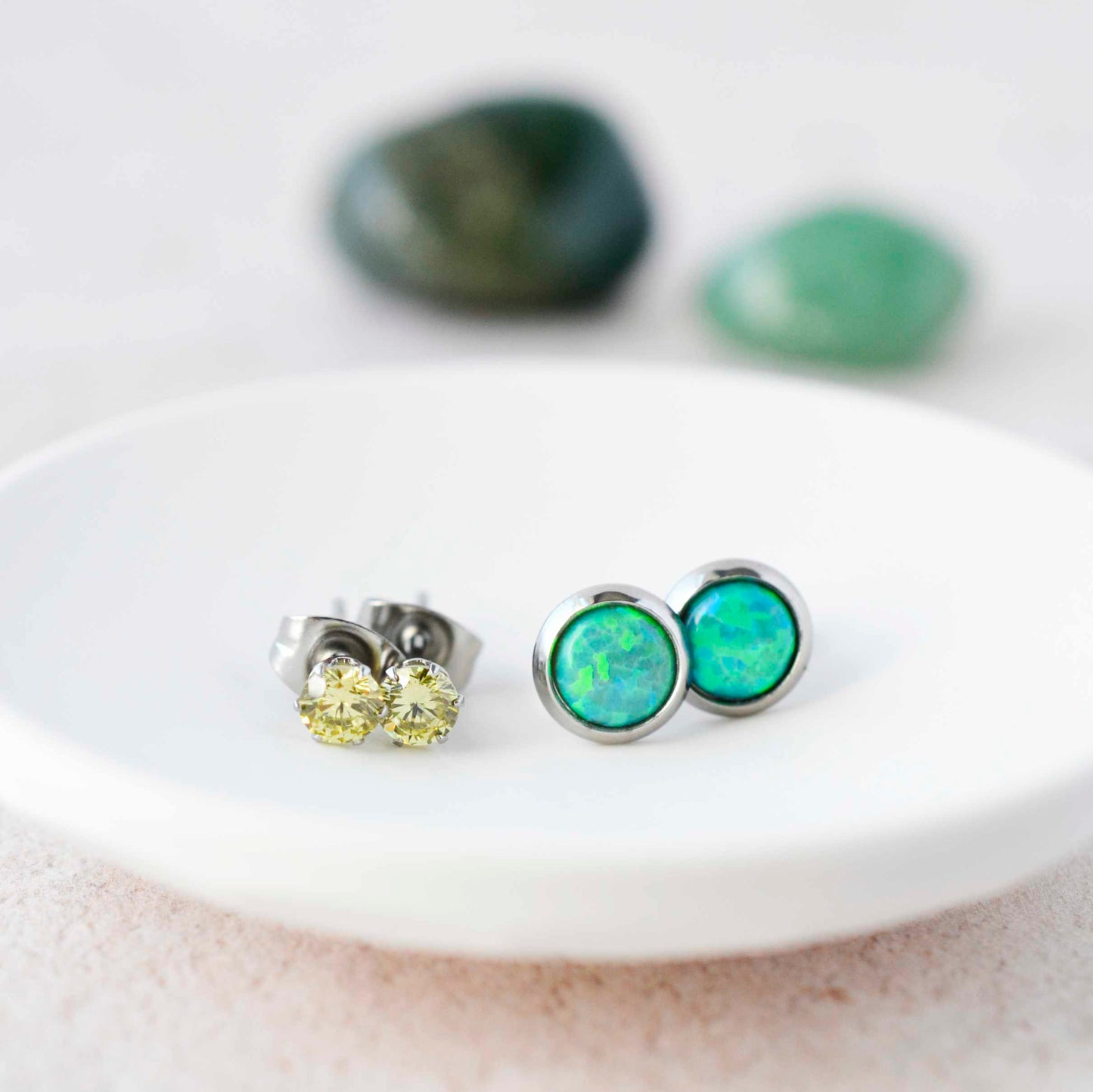 Green CZ studs and green lab opal stud earrings sitting in a small white trinket dish.