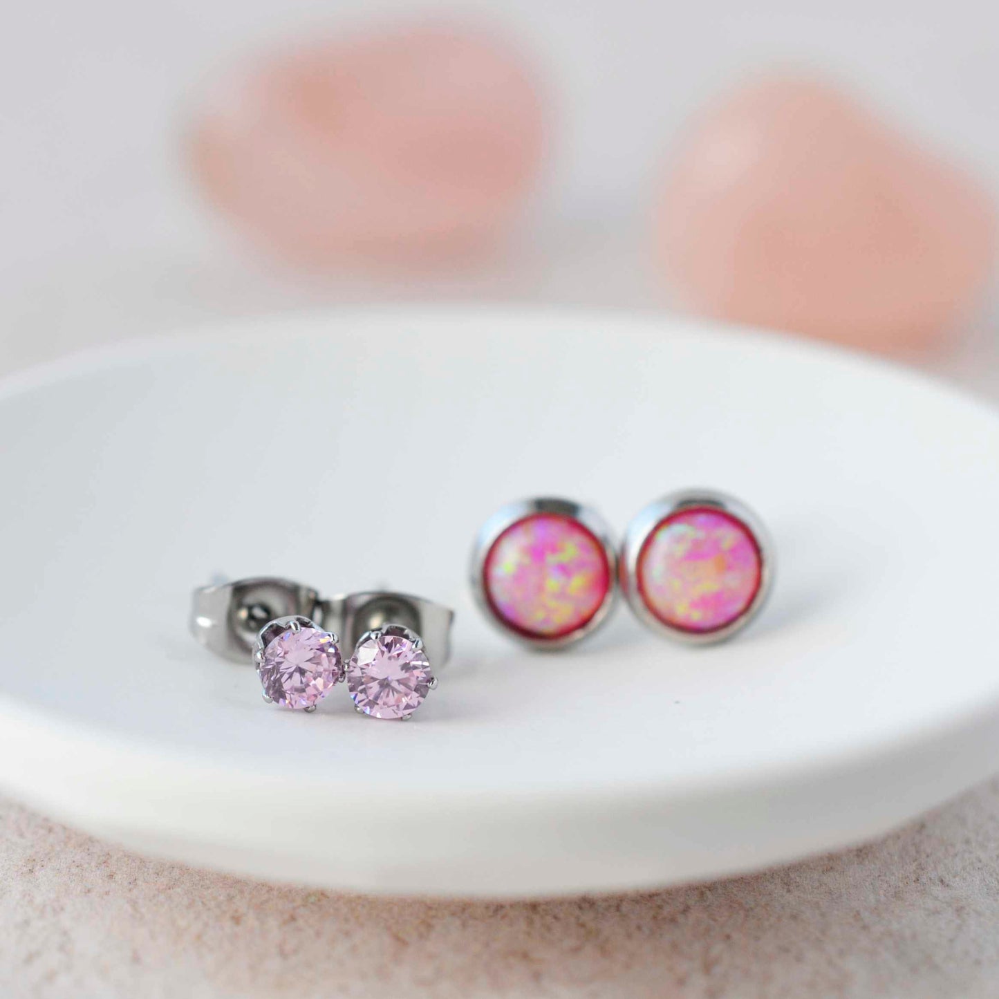 Pink CZ studs and pink lab opal stud earrings sitting in a small white trinket dish.
