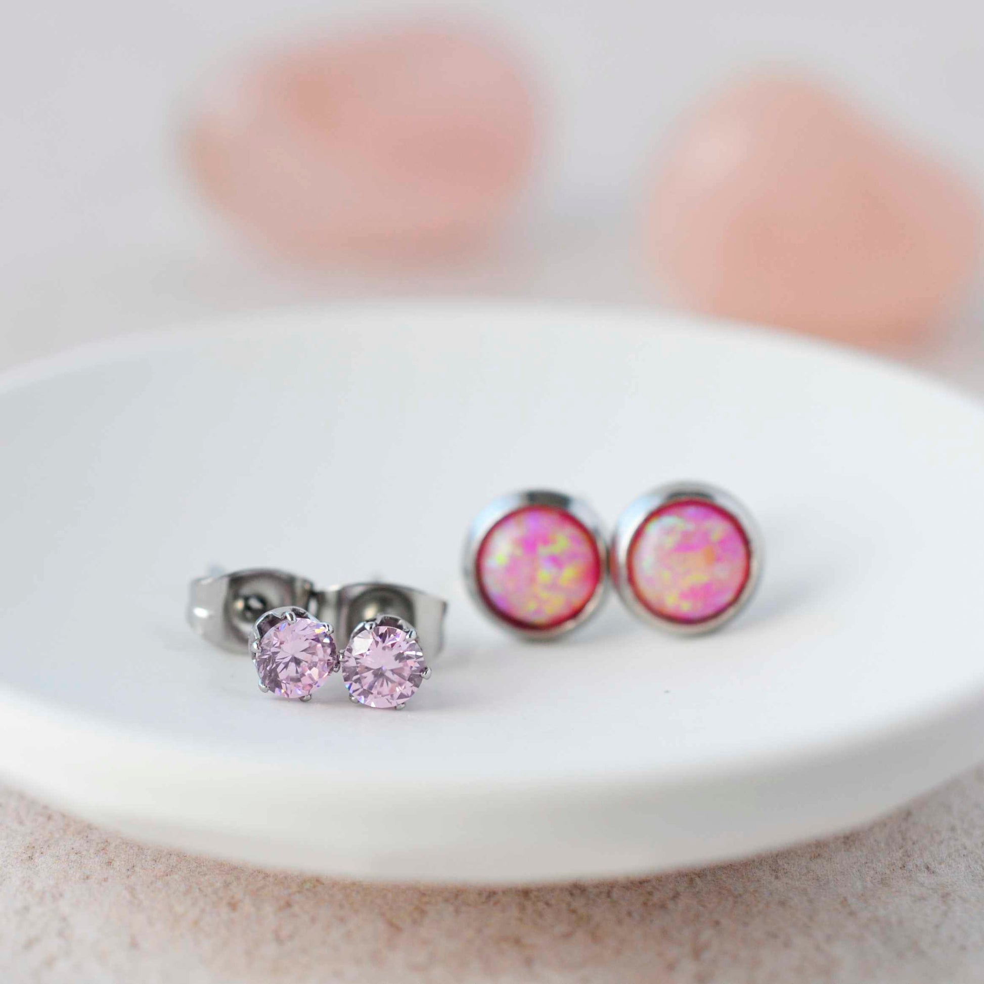 Pink CZ studs and pink lab opal stud earrings sitting in a small white trinket dish.