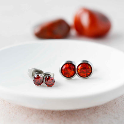 Red CZ studs and red lab opal stud earrings sitting in a white trinket dish.