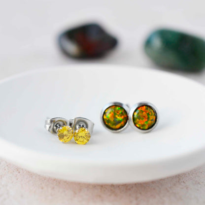 Small yellow CZ and olive green lab opal stone stud earrings sitting in a white trinket dish.