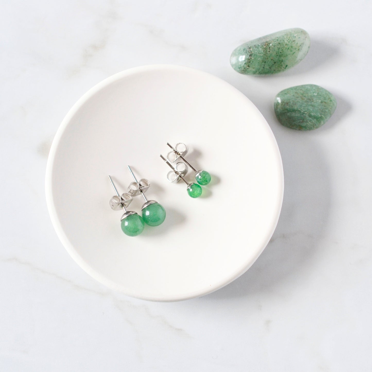 Green earrings on a white trinket dish with green stones on a light gray background