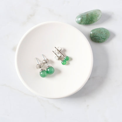 Green earrings on a white trinket dish with green stones on a light gray background