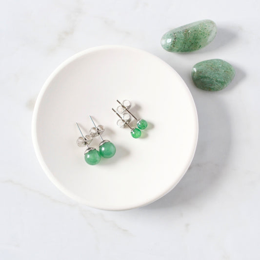 Green earrings on a white trinket dish with green stones on a light gray background