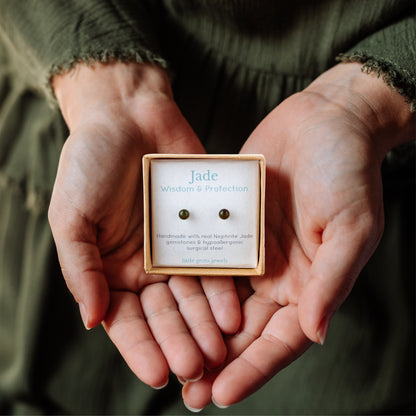 Hands holding small square eco-friendly gift box containing tiny Jade gemstone earrings.