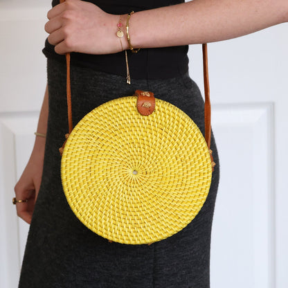 Yellow round woven bag held by a person against a white background
