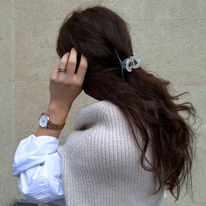 Person with a ponytail wearing a watch, standing against a beige wall.