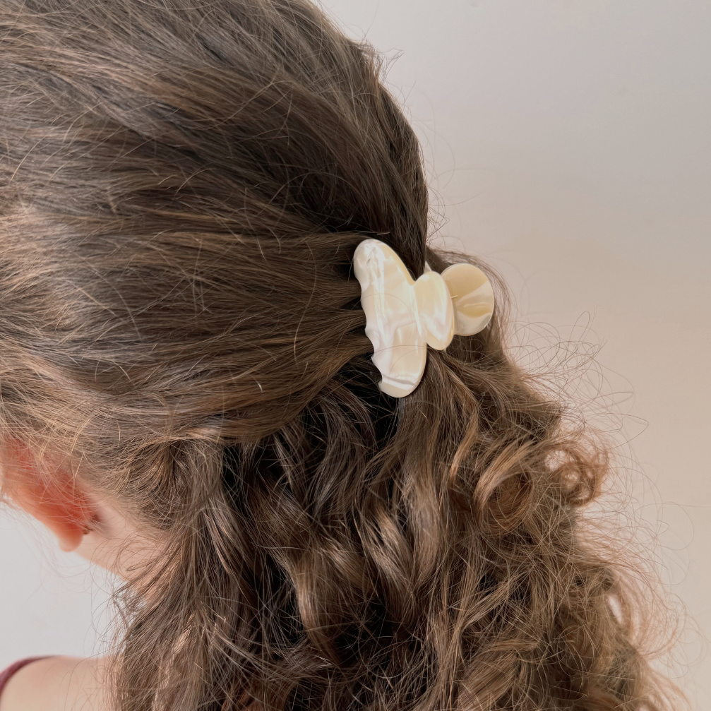 Close-up of a girl with curly hair wearing a beige butterfly hair clip against a neutral background