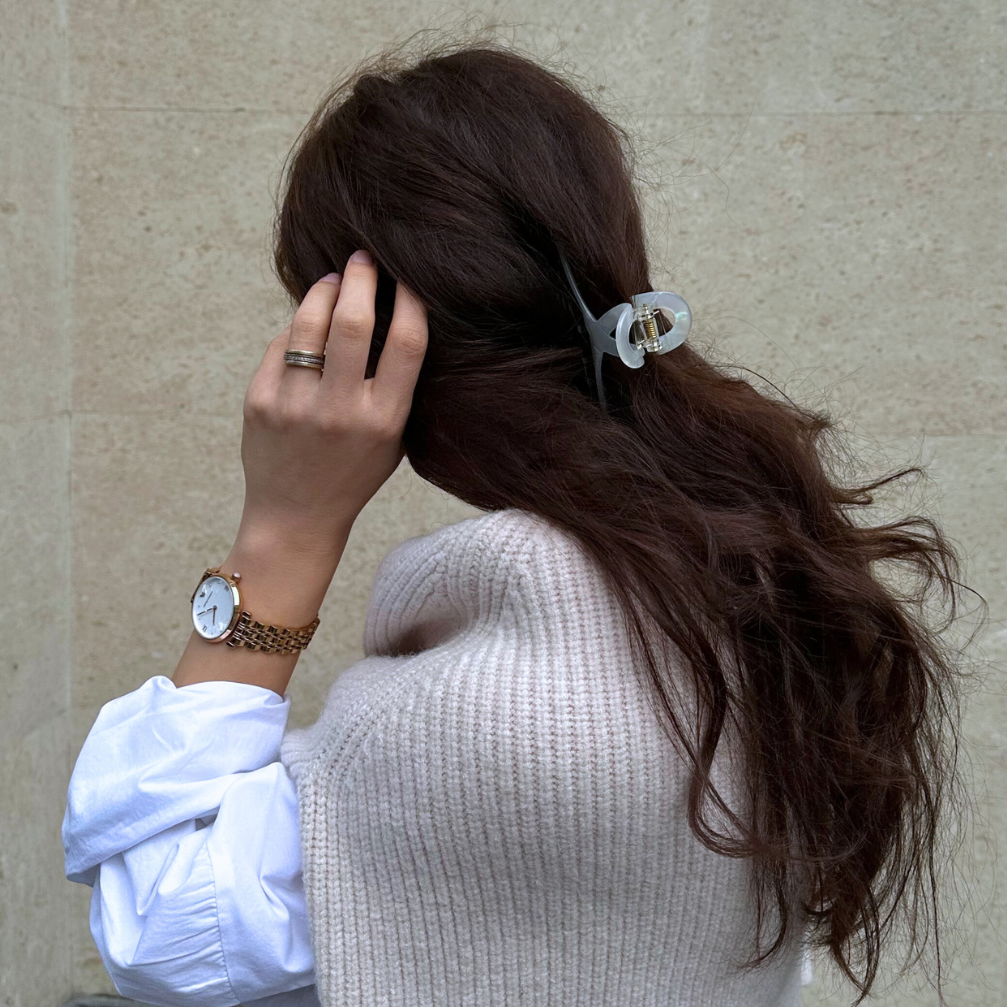 Person with a ponytail wearing a watch, standing against a beige wall.