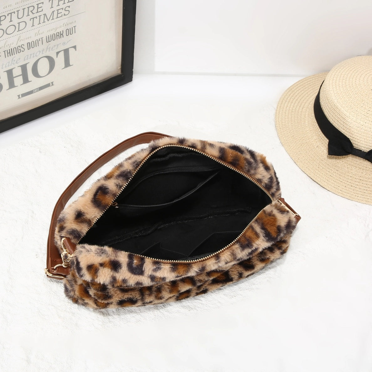Top view of open Leopard print clutch bag on a white surface with a hat in the background
