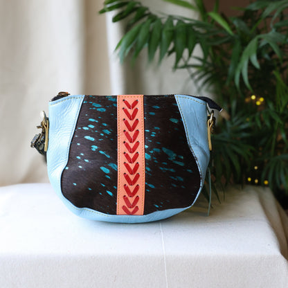 Handbag with black, blue, and pink design on a white surface with a plant in the background
