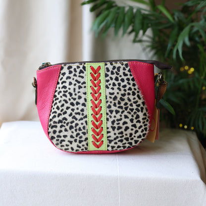 Small handbag with leopard print and pink accents on a white surface with a plant in the background