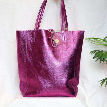 Purple metallic tote bag on a white background with a plant in the corner
