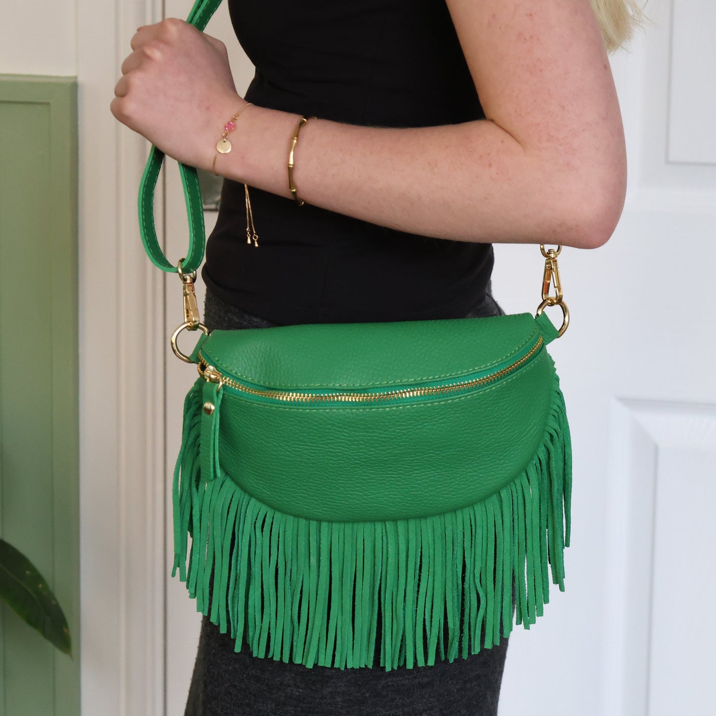 Green fringed handbag held by a person against a white door background