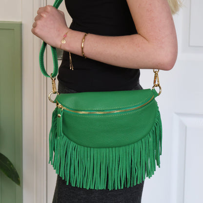 Green fringed handbag held by a person against a white door background