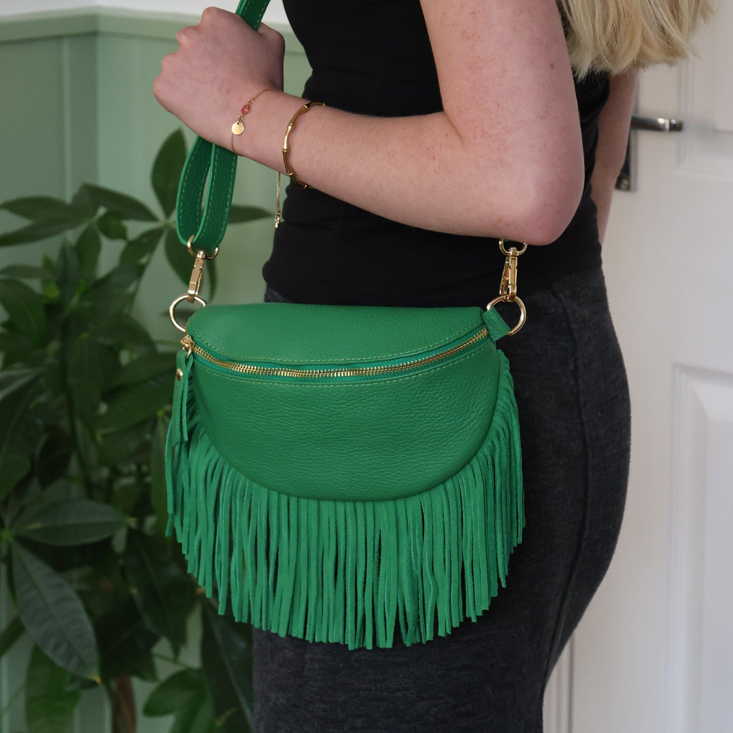 Green fringed handbag held by a person against a light green wall.