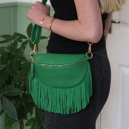 Green fringed handbag held by a person against a light green wall.