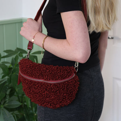 Person holding a red textured handbag with a plant in the background