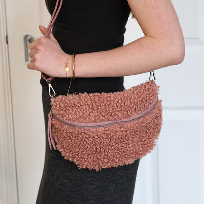 Person holding a pink fuzzy crossbody bag in front of a white door.